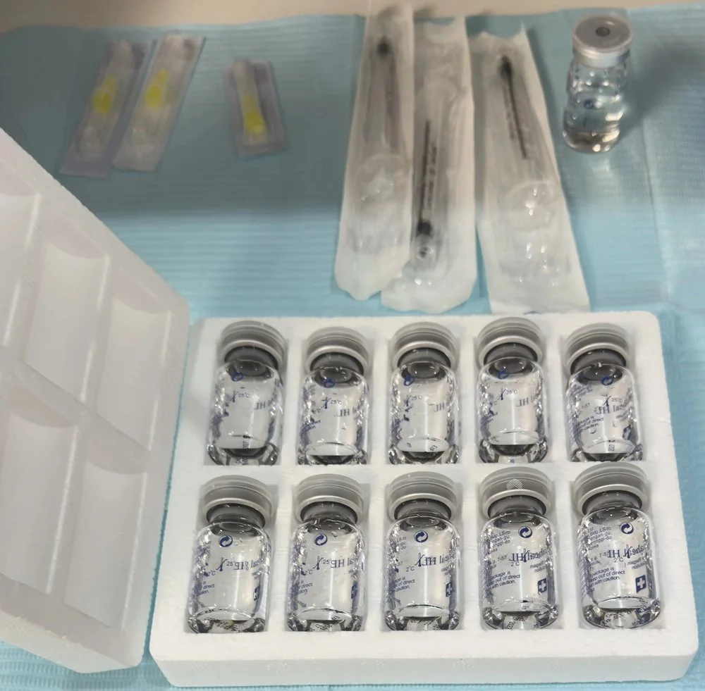 A tray of ten sealed glass vials of clear treatment solution, beside sterile packaged syringes and needles ready for use